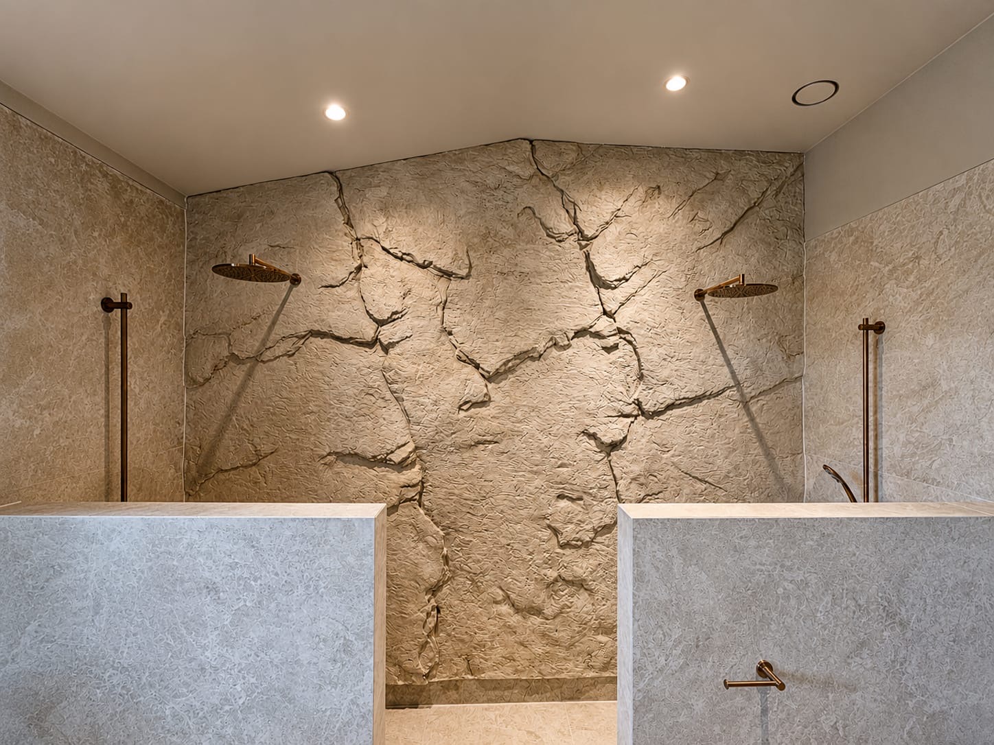 Badkamer met natuursteen reliëfwand, marmerlook tegels en bronzen regendouches